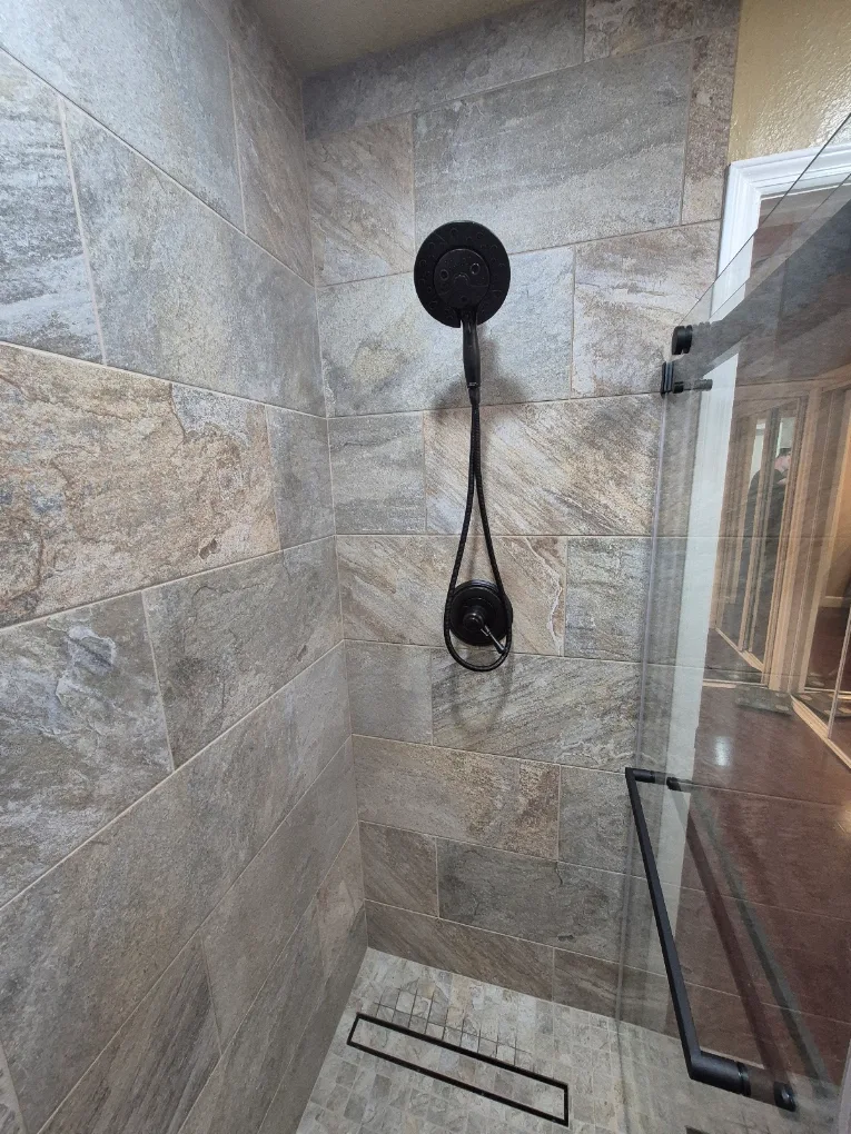 Walk-in shower with matte black fixtures, stone-look tile, and a linear drain