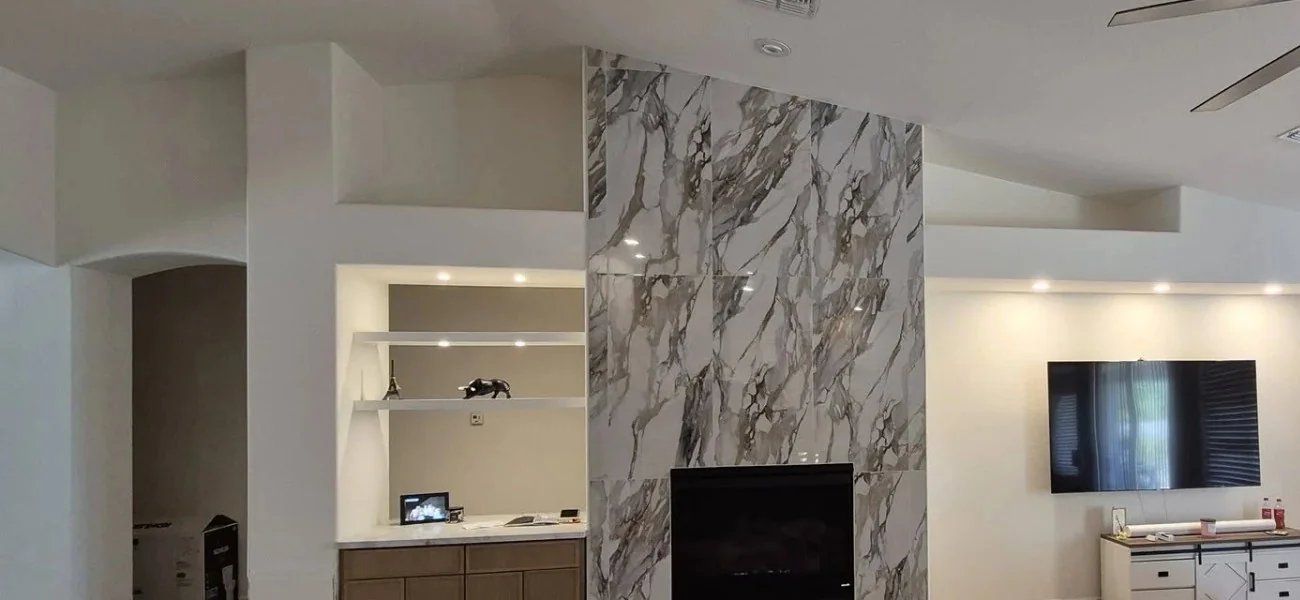 Remodeled living room with a floor-to-ceiling marble fireplace, built-in bar shelving, a vaulted ceiling, and a wall-mounted television
