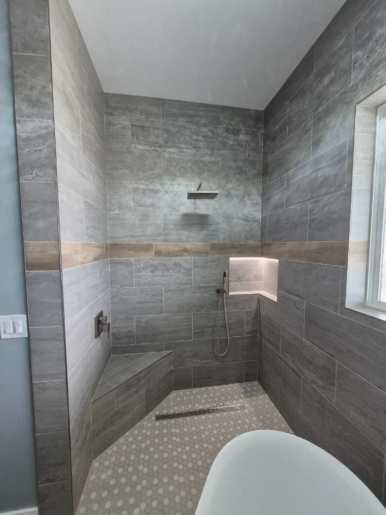 Finished tile shower with corner bench, lit niche, and linear drain
