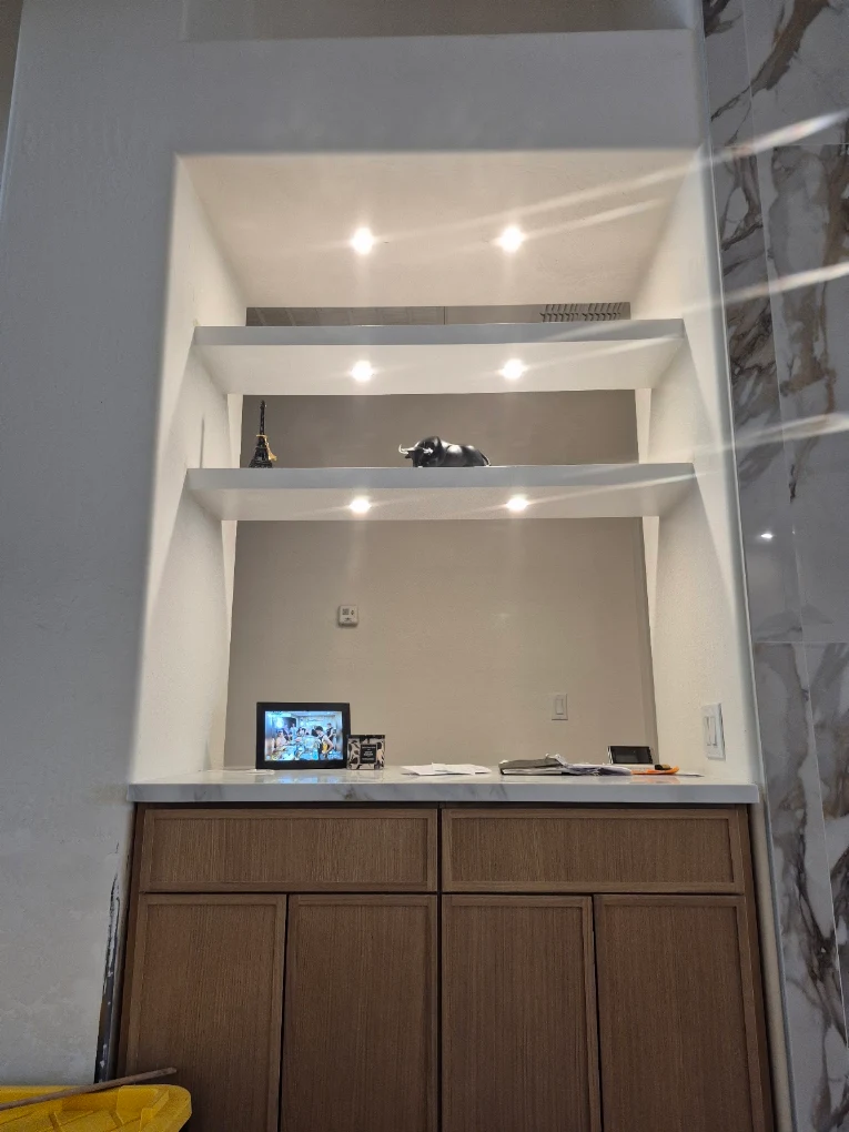 Built-in alcove with light oak cabinets, white counters, and lit floating shelves