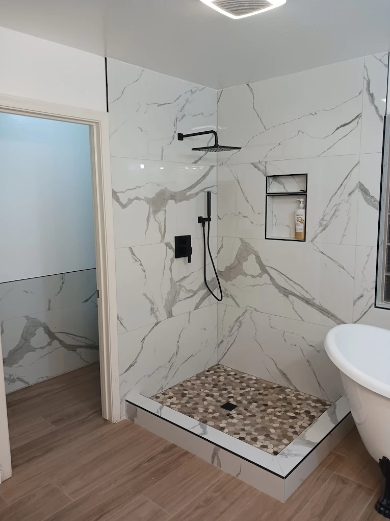 Walk-in shower with marble-look tile, matte black shower head, and pebble tile floor