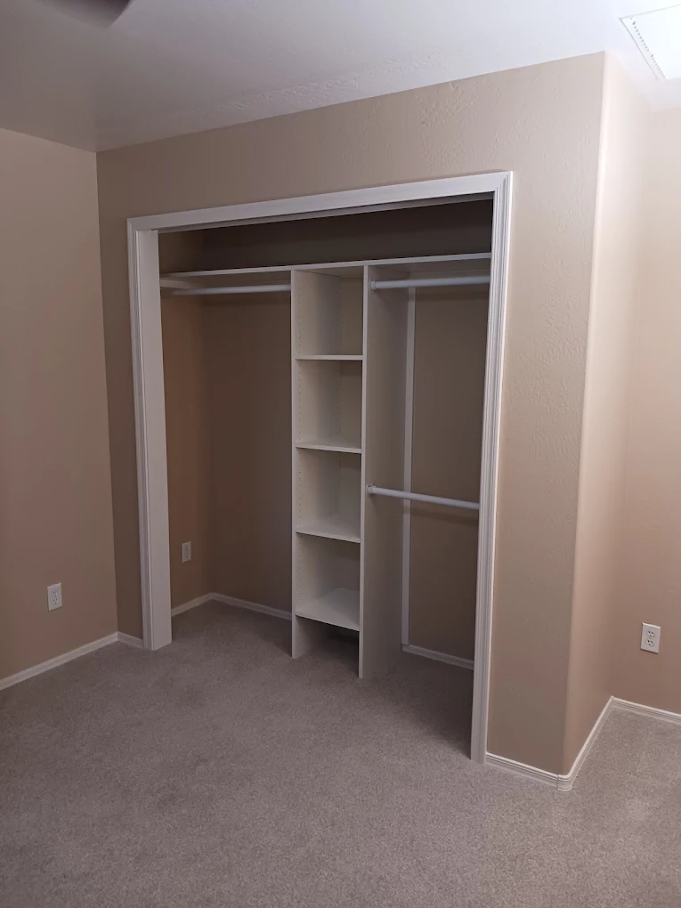 Bedroom closet fitted with a white organizer system of shelves and hanging rods