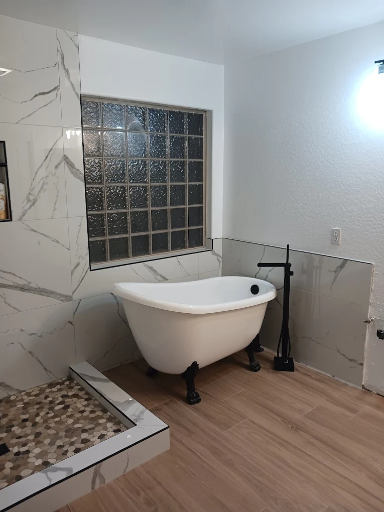 Bathroom with a black clawfoot tub, marble-look tile, and a glass block window