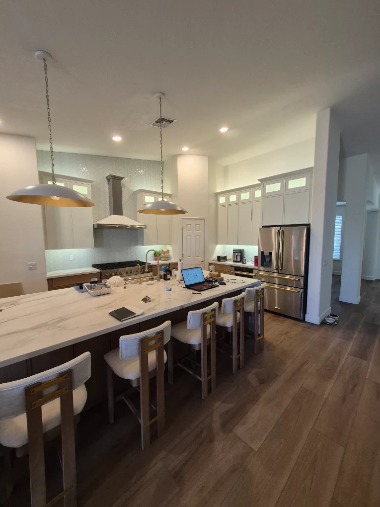 Completed kitchen remodel with white cabinetry, marble-look island, and gold pendant lighting